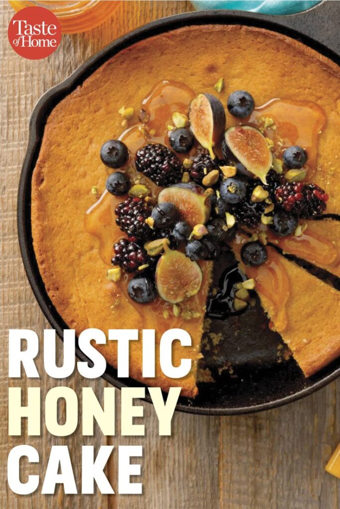 Rustic honey cake topped with fresh figs, berries, and nuts in a skillet, ideal for cozy homemade dessert.