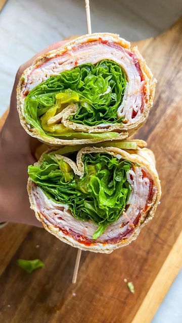 Close-up of a fresh deli wrap with turkey, lettuce, and peppers, held in hand on a wooden board.