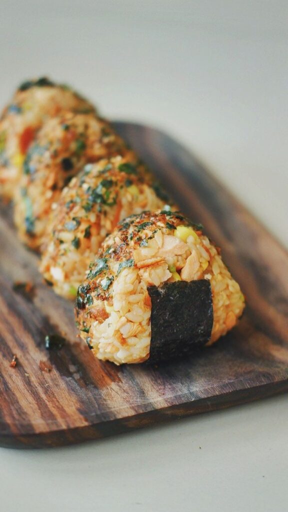 Delicious homemade onigiri with seaweed and herbs, served on a rustic wooden board. Traditional Japanese rice balls.