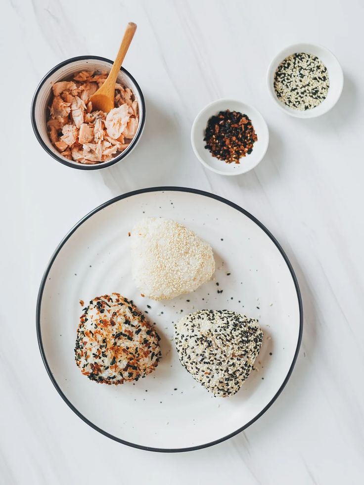 Trio of seasoned rice balls with salmon, sesame seeds, and spices on a white plate, ideal for a Japanese-inspired meal.