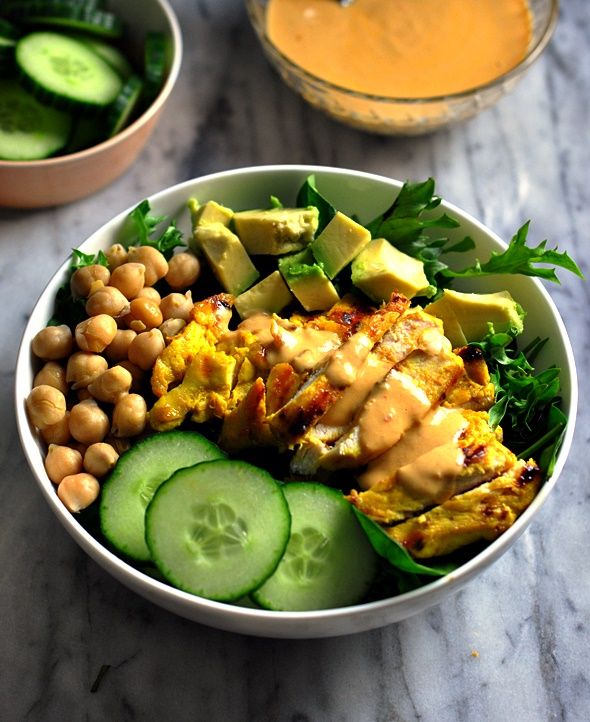 Chicken salad bowl with cucumber, avocado, chickpeas, and dressing, served on a marble surface.