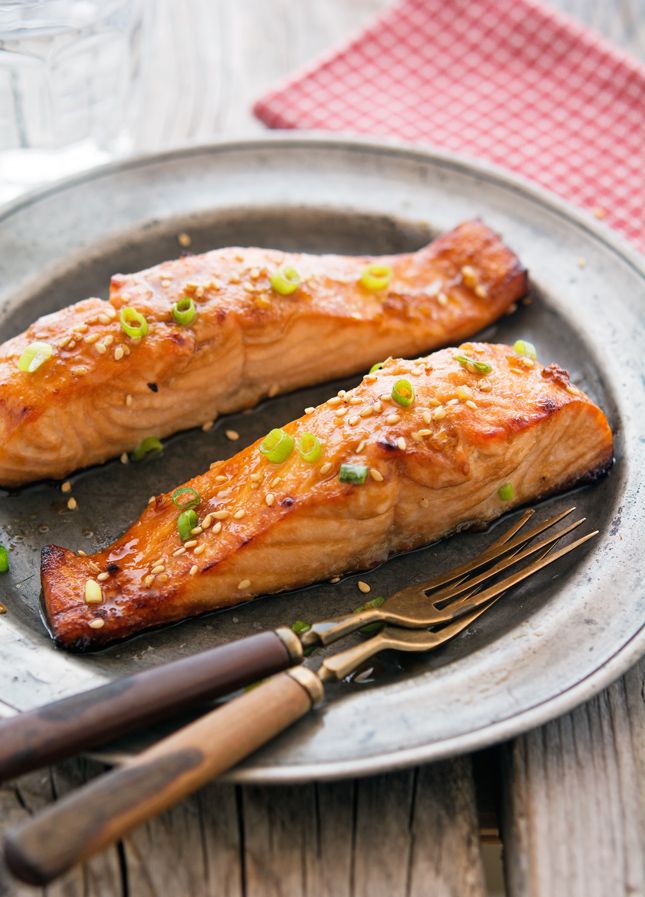 Grilled salmon fillets garnished with green onions and sesame seeds on a round plate with cutlery.