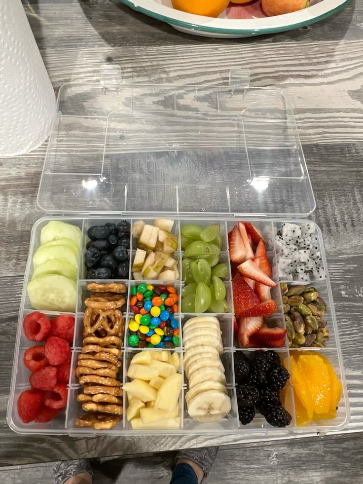 Colorful snack box filled with fruits, pretzels, and candy on a wooden table, offering a variety of healthy choices.