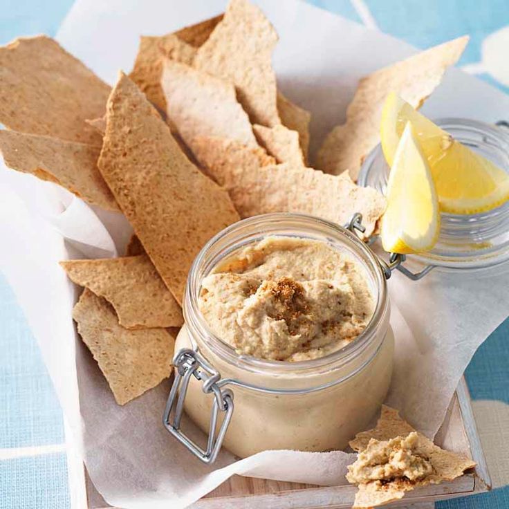 Jar of hummus with pita chips and lemon wedges, served on a parchment-lined tray.
