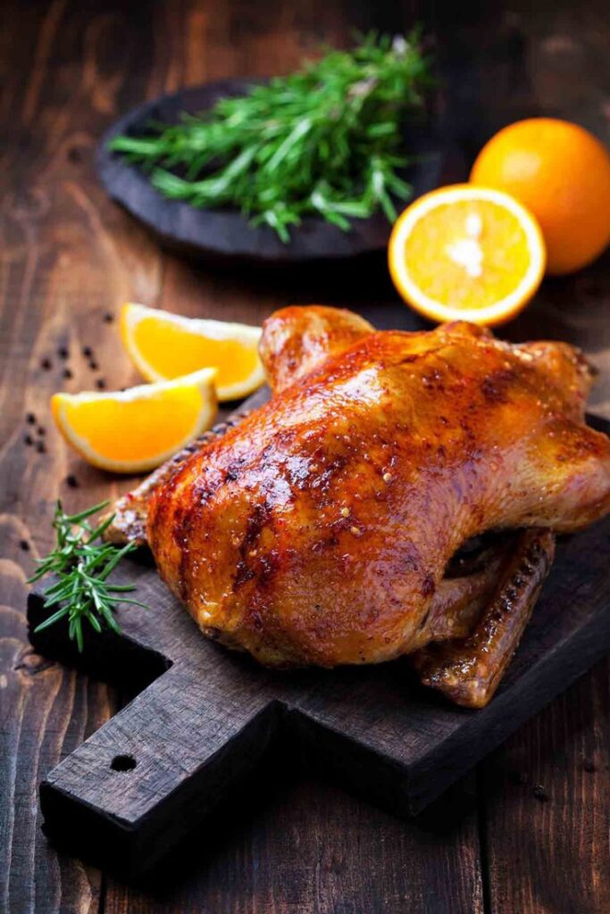 Roast chicken on a wooden board with orange slices and rosemary garnish, perfect for dinner recipes.
