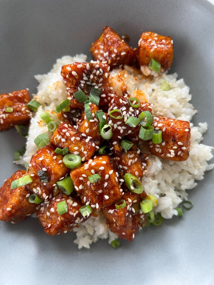 Spicy sesame tofu with green onions over white rice in a bowl, garnished with sesame seeds.