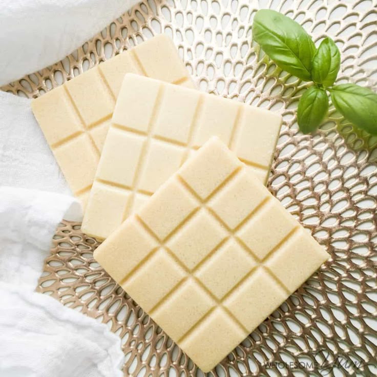 Three white chocolate bars on a textured tray with basil garnish, accompanied by a white cloth for an elegant presentation.