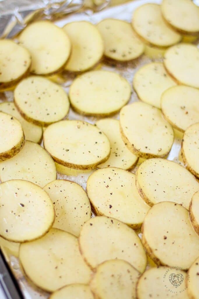 Sliced potatoes seasoned with pepper on a baking sheet, ready to be roasted for a delicious side dish.