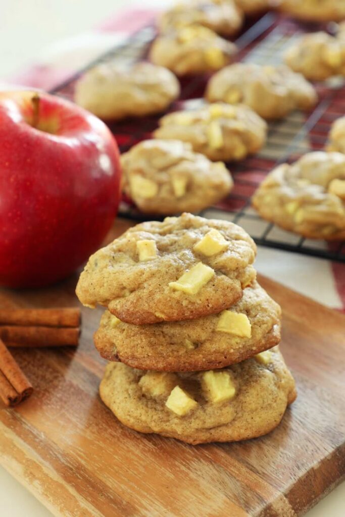 Homemade apple cinnamon cookies stacked with fresh apple and cinnamon sticks in the background.