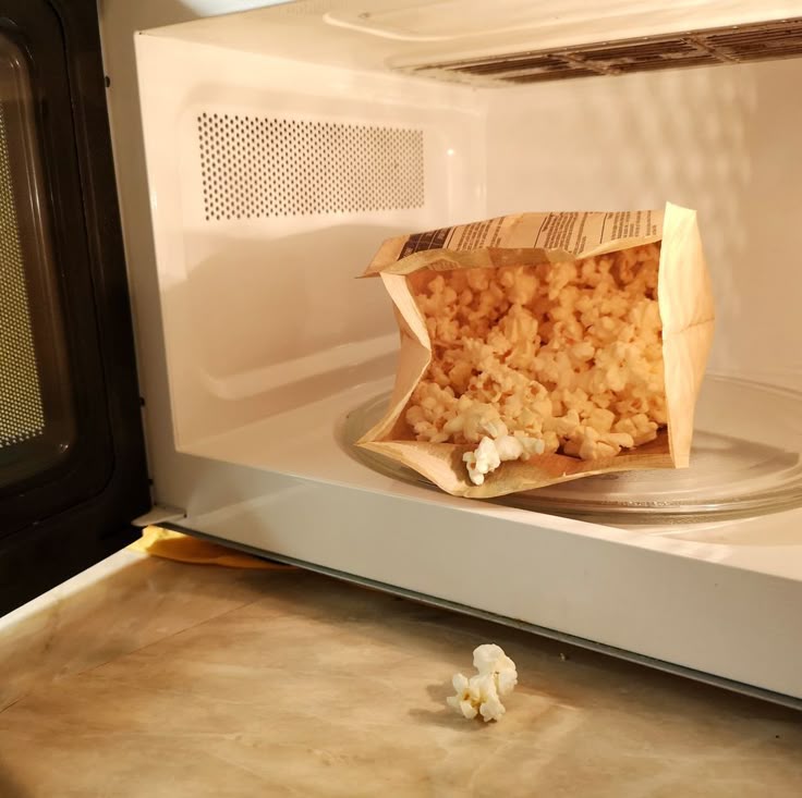Microwave with open bag of popcorn, kernels spilled on the counter, depicting a kitchen snack scene.