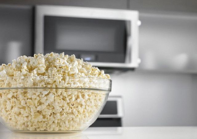 Bowl of fresh popcorn with microwave in the background, ideal for movie nights or snack time at home.