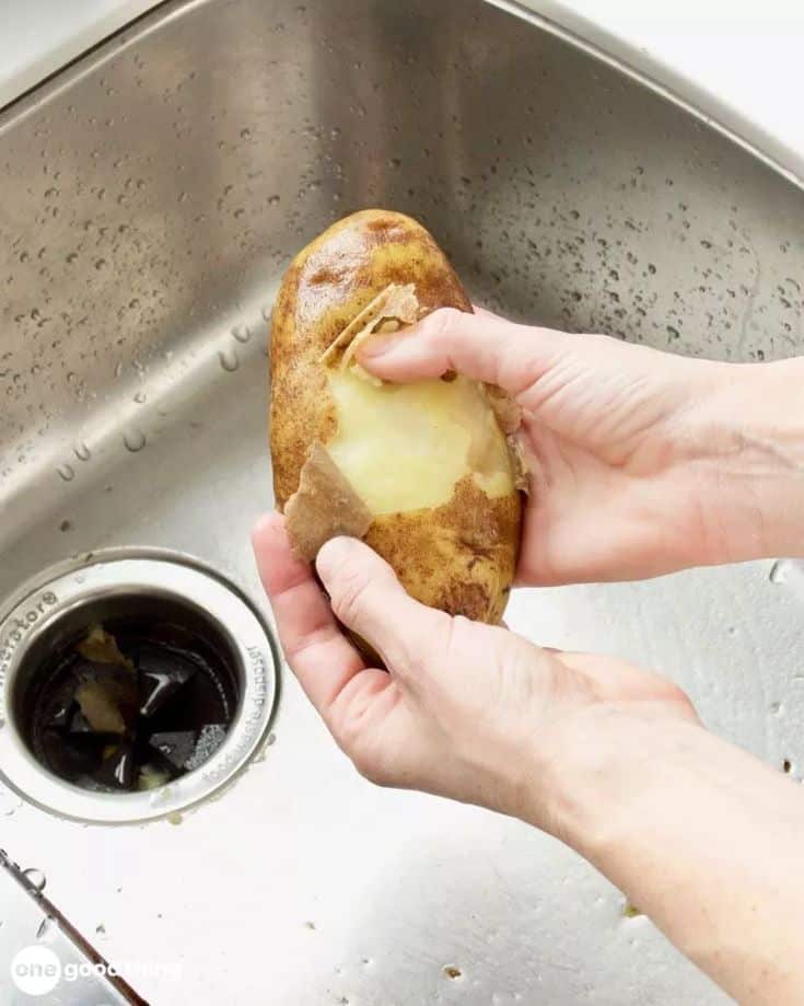 Peeling a boiled potato over a kitchen sink, showing an easy skin removal method.