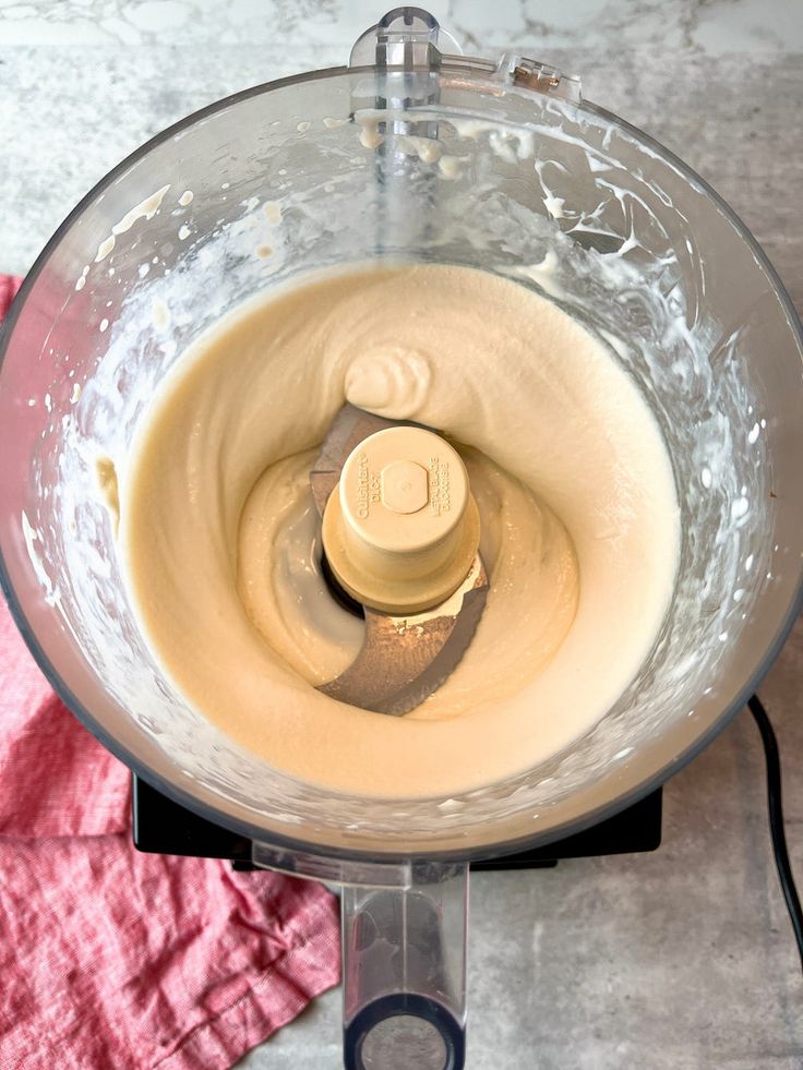 Smooth hummus being blended in a food processor on a kitchen counter.