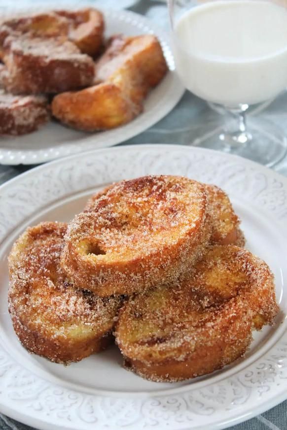 Plate of golden, sugared French toast with glass of milk on a white tablecloth.