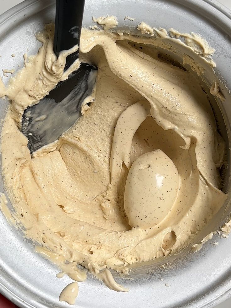 Creamy vanilla bean ice cream mixture in a churn, ready to freeze with a spatula for stirring.