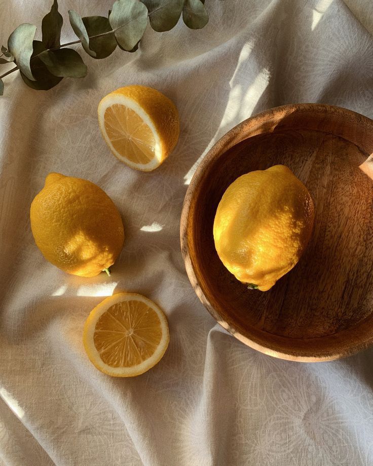 Fresh lemons in a wooden bowl on a sunlit fabric, accompanied by eucalyptus leaves.
