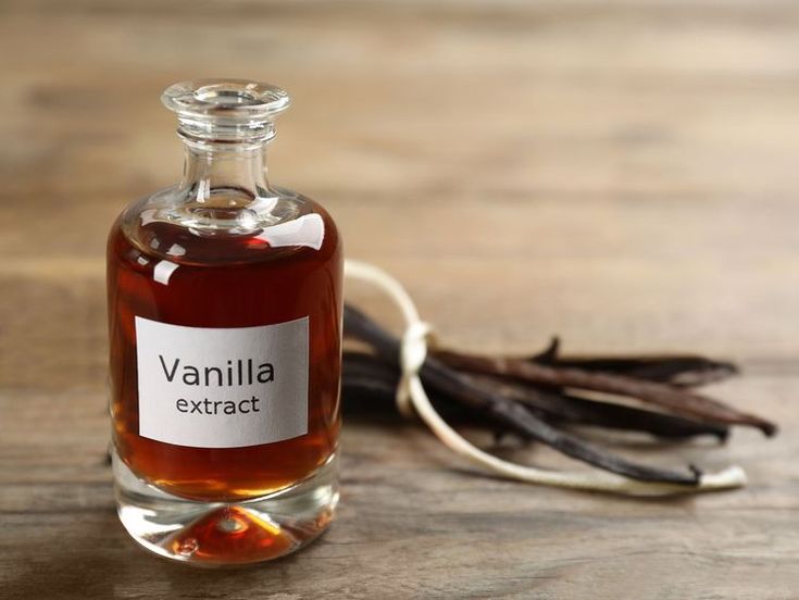 Glass bottle of vanilla extract with vanilla beans on a wooden surface. Perfect for baking and flavoring recipes.
