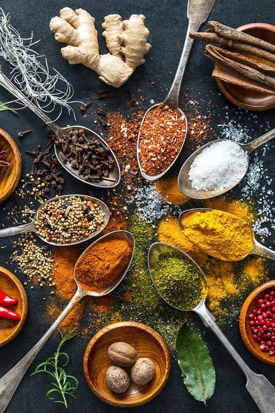 Assorted spices and herbs on spoons and bowls, featuring turmeric, ginger, and pepper, on a dark background.