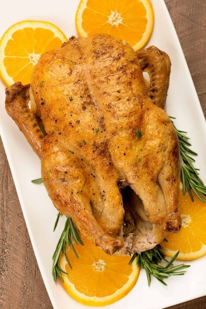 Roast chicken garnished with fresh orange slices and rosemary on a white platter.