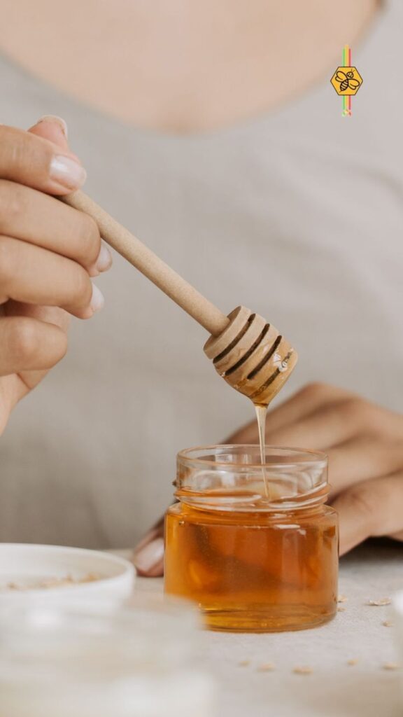 Person drizzling honey into a jar using a wooden dipper, showcasing natural sweetness.