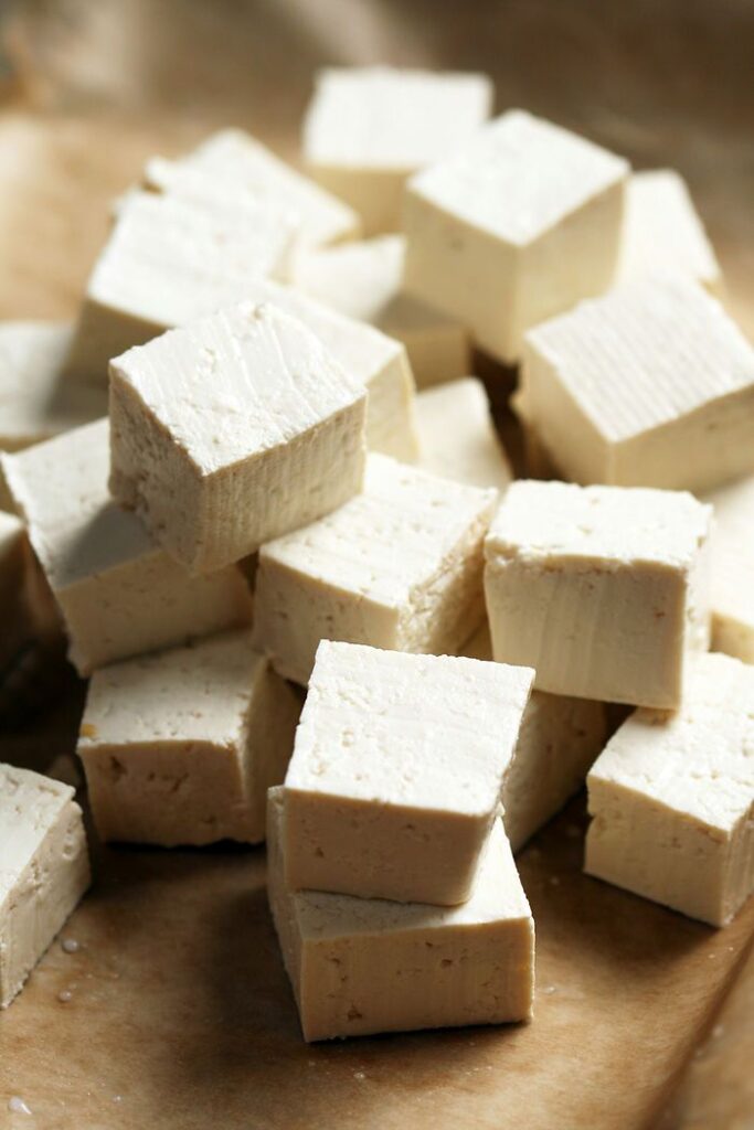Cubes of fresh tofu stacked on parchment paper, ready for cooking or adding to a vegan dish.