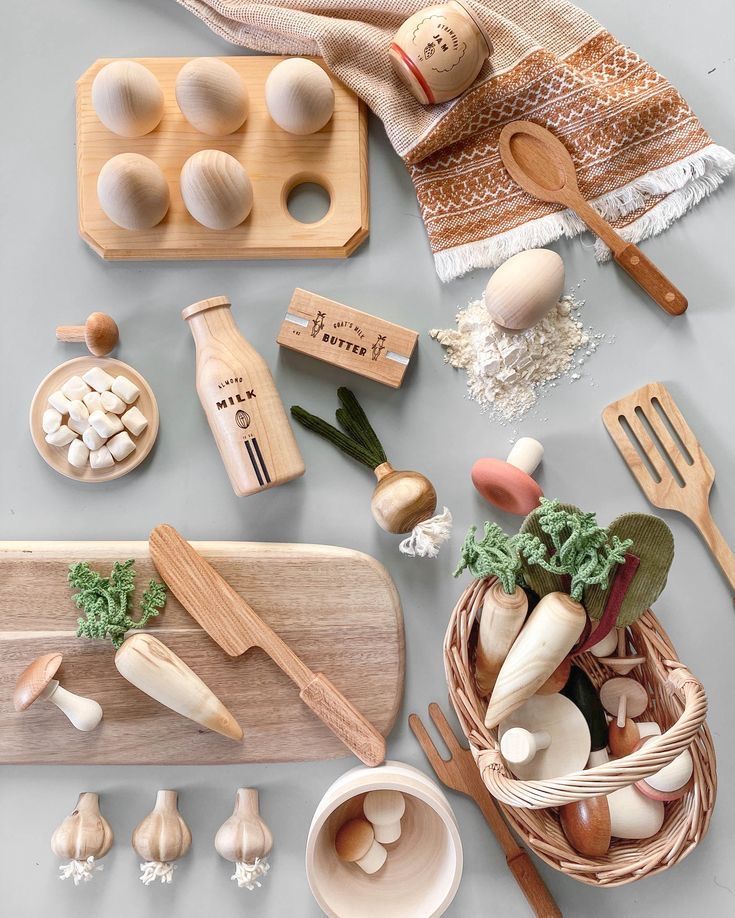 Wooden toy kitchen set with fruits, vegetables, eggs, milk, butter, and utensils arranged on a rustic table.