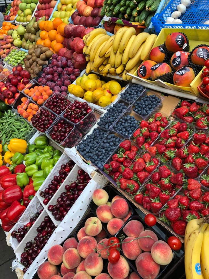 Fresh fruits and vegetables display with bananas, berries, bell peppers, peaches, and more at a vibrant market stall.