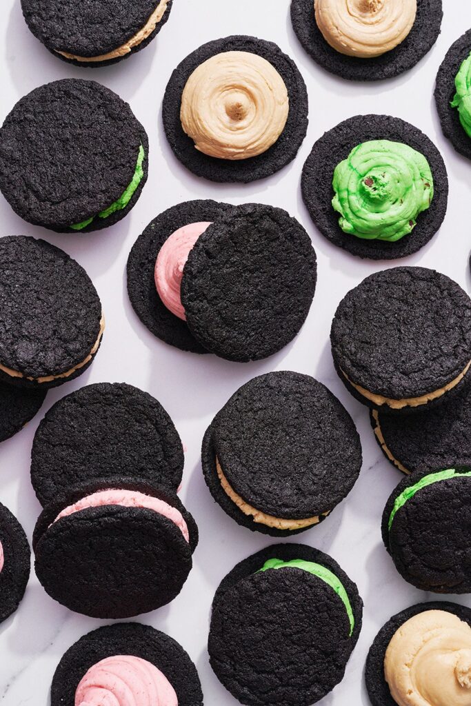 Assorted black sandwich cookies with colorful cream fillings on a white background.