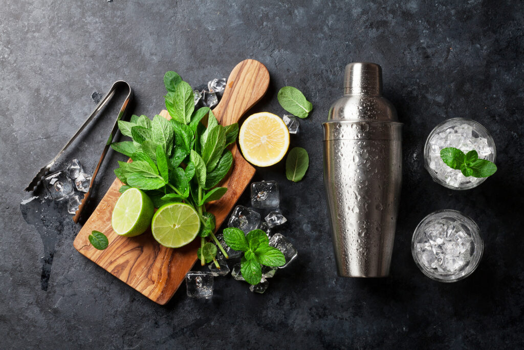 Mint, lime, lemon, ice, and shaker on slate background ready for cocktail preparation.