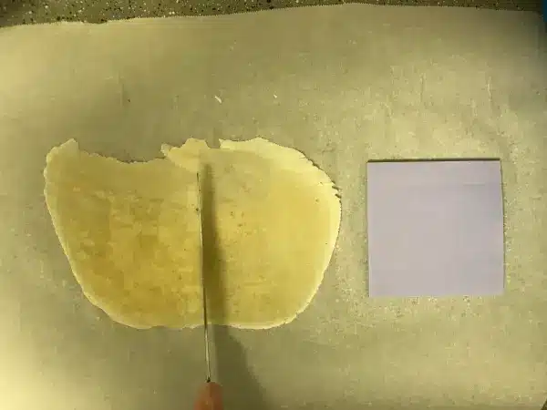 A knife slicing through rolled dough on parchment paper, with a square blue note beside it.