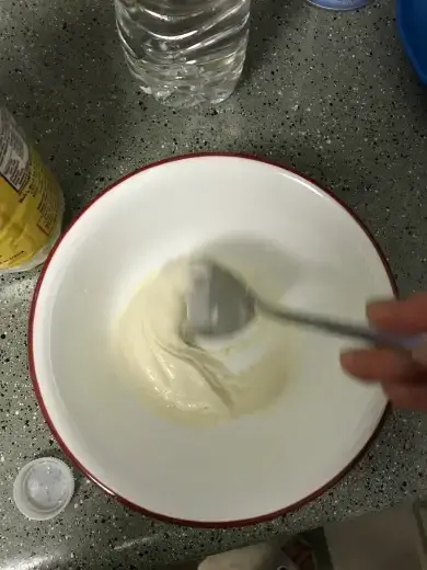 Mixing batter with a spoon in a white bowl on a speckled countertop.