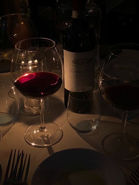 Candlelit dinner with red wine glasses and bottle on a table, creating an intimate and cozy atmosphere.
