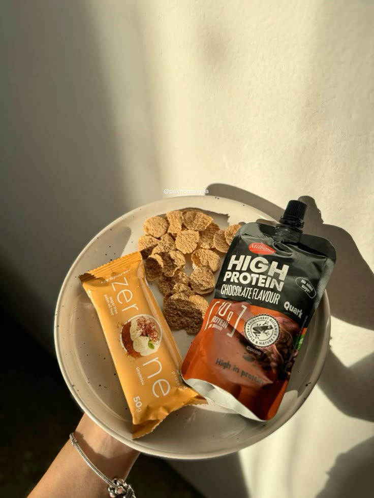 Bowl with cereal, a protein chocolate pouch, and a bar. Healthy breakfast with high protein snacks in sunlight.
