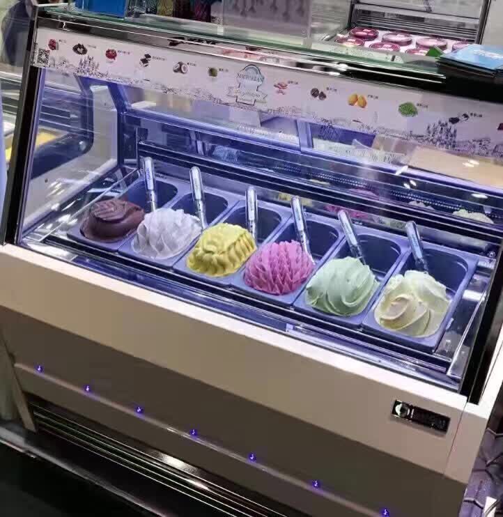 Gelato flavors on display in an ice cream parlor, featuring chocolate, vanilla, strawberry, and pistachio.