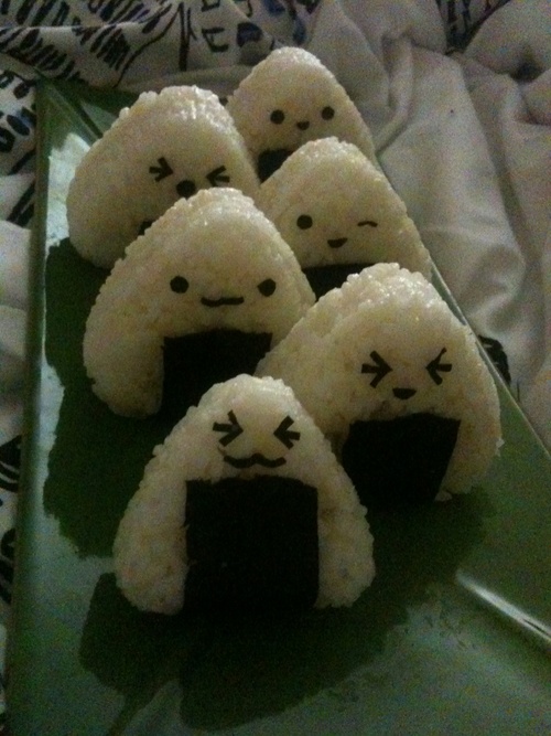 Cute onigiri rice balls with seaweed and adorable faces on a green plate, ideal for a fun Japanese-themed meal.