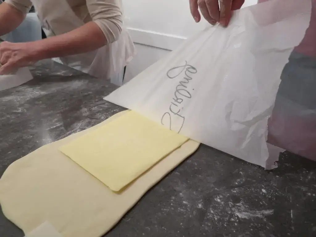 Person preparing pastry dough with butter on a floured surface in a kitchen setting.