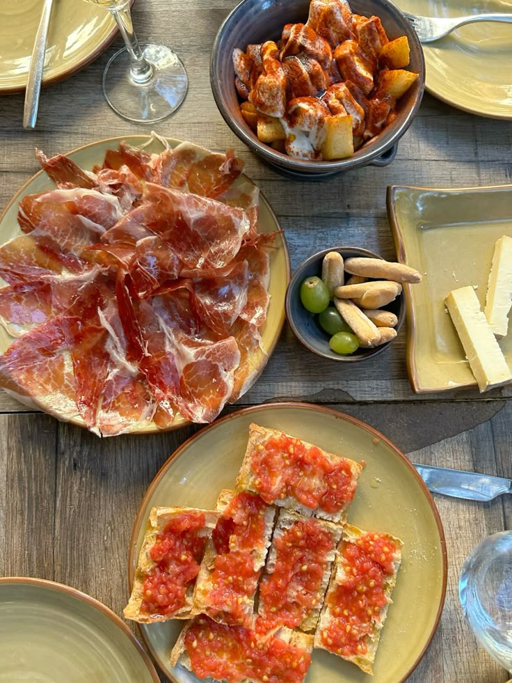 Spanish tapas spread with jamón, patatas bravas, and pan con tomate on a wooden table.