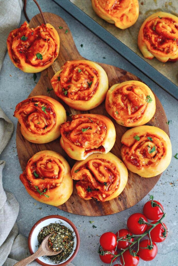 Freshly baked pizza rolls with tomato sauce and herbs on a wooden board, garnished with fresh cherry tomatoes.