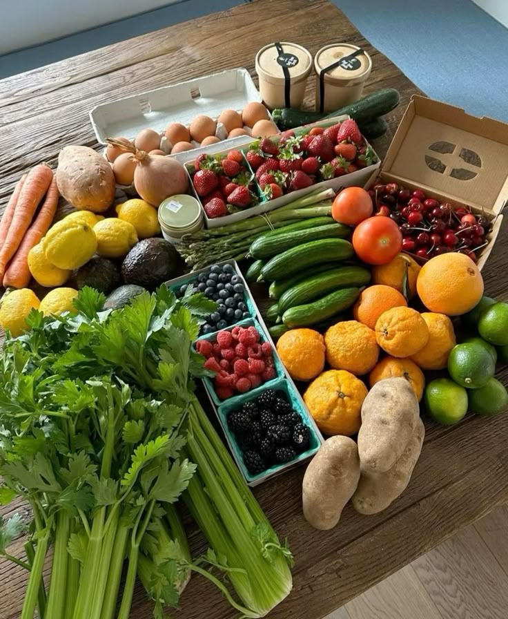 Assorted fresh fruits and vegetables arranged on a wooden table, including strawberries, oranges, and celery.