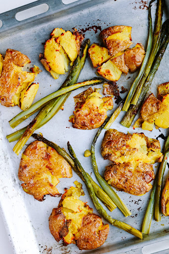 Roasted smashed potatoes with green onions on a baking sheet. Crispy and golden for a delicious side dish.