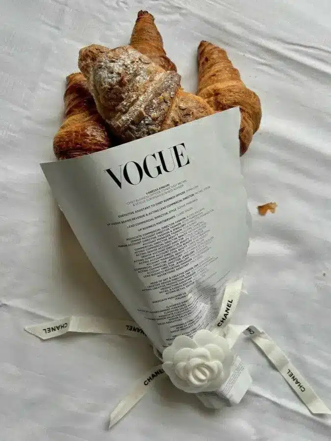 Croissants wrapped in Vogue paper with Chanel ribbon on white cloth background.