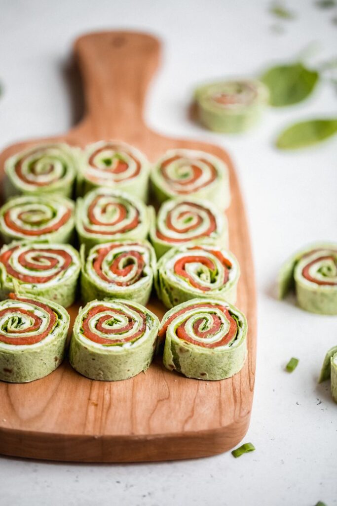Fresh spinach and salmon pinwheels arranged on a wooden board, perfect for a healthy appetizer.