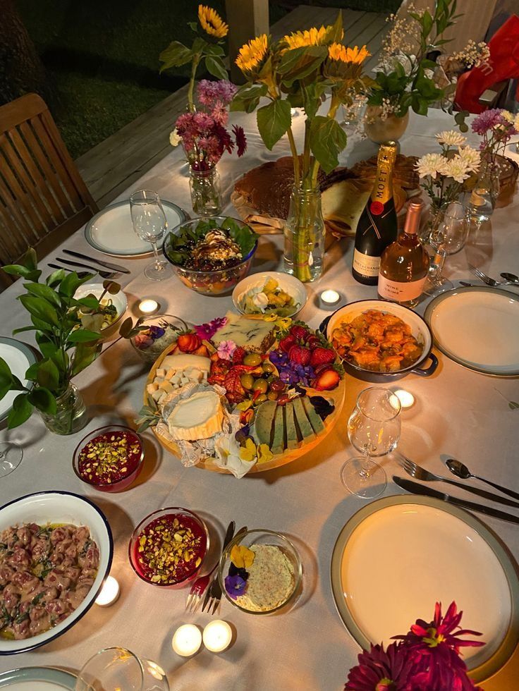 Elegant dinner table setting with candles, flowers, cheese board, vibrant dishes, and wine for a cozy evening gathering.