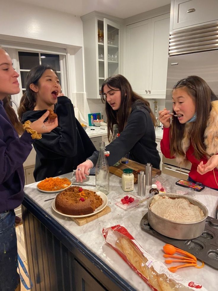 Friends enjoying dessert in a kitchen with cakes and snacks on a marble countertop.