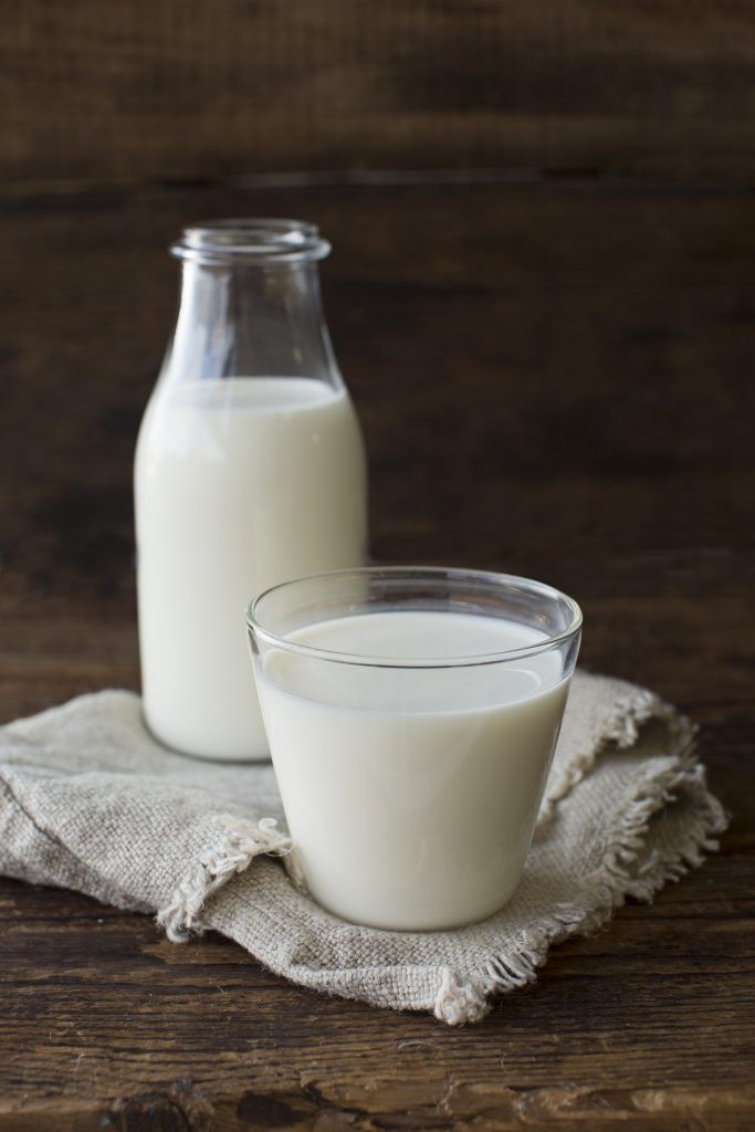 Glass and bottle of fresh milk on rustic wooden table with linen cloth background. Perfect for dairy concept.