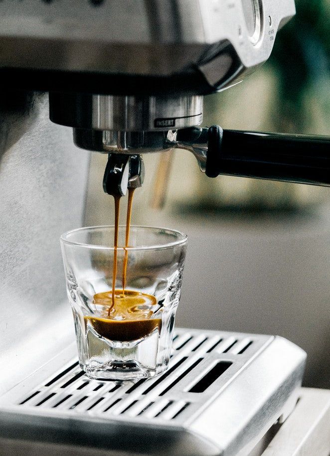 Espresso machine pouring fresh coffee into a glass cup, close-up shot.