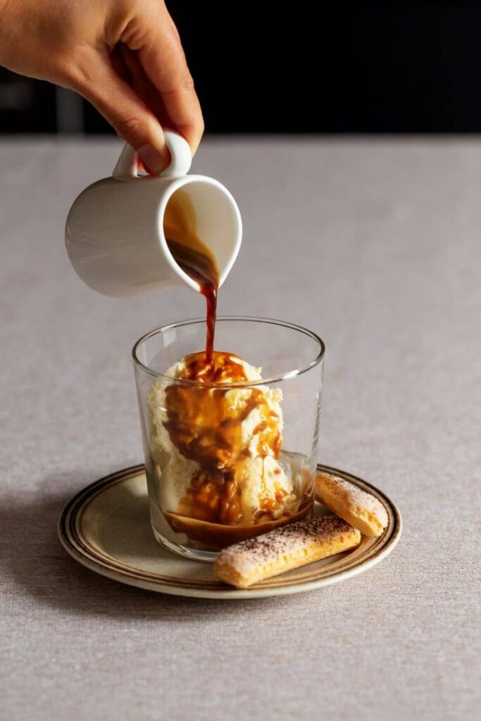 Affogato served in a glass with espresso poured over vanilla ice cream, accompanied by ladyfingers on a plate.