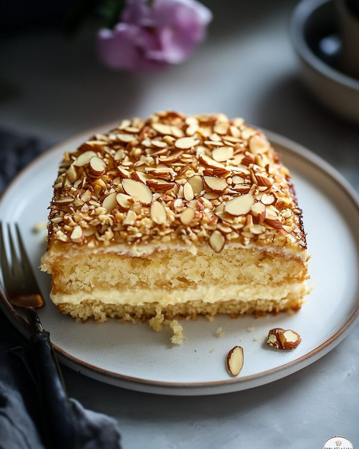 Slice of almond cake with creamy layers on a plate, garnished with sliced almonds. Perfect dessert for any occasion.