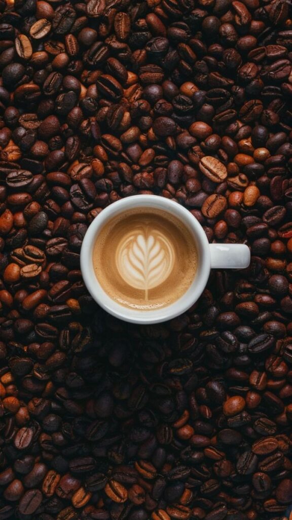 A cup of latte with leaf art, surrounded by rich roasted coffee beans, showcasing barista skills and coffee passion.
