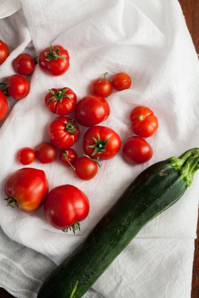 Fresh tomatoes and zucchini on a white cloth, showcasing vibrant colors and healthy garden produce.